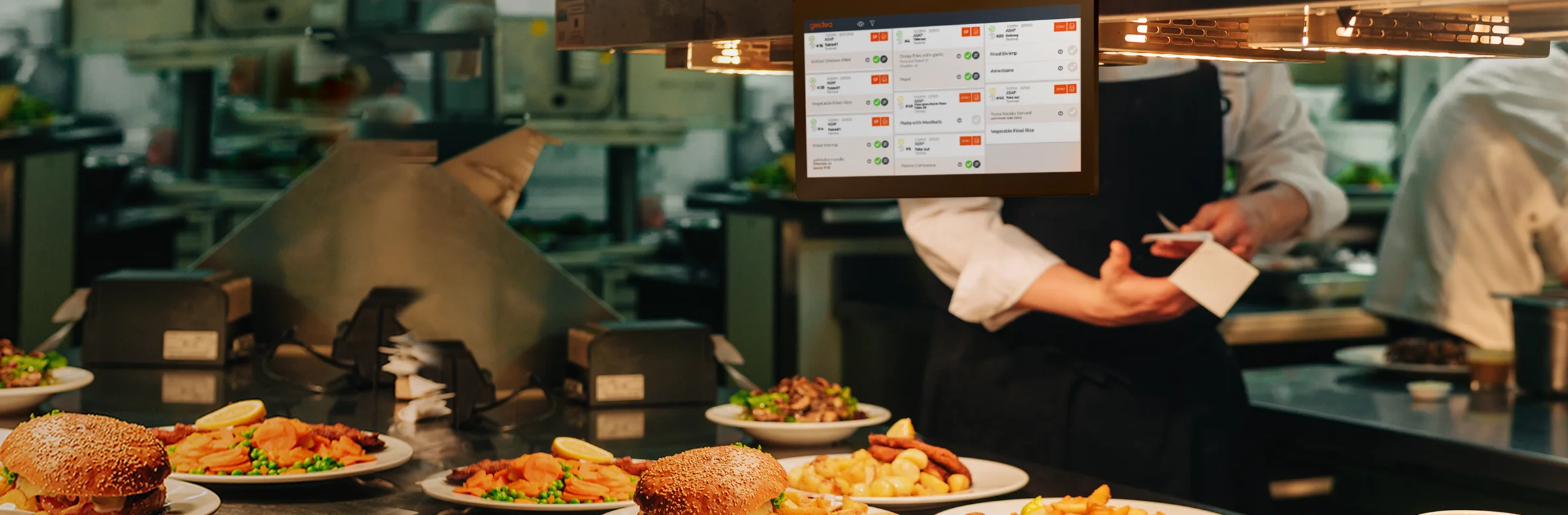 Busy kitchen pass with a kitchen display above plating stations