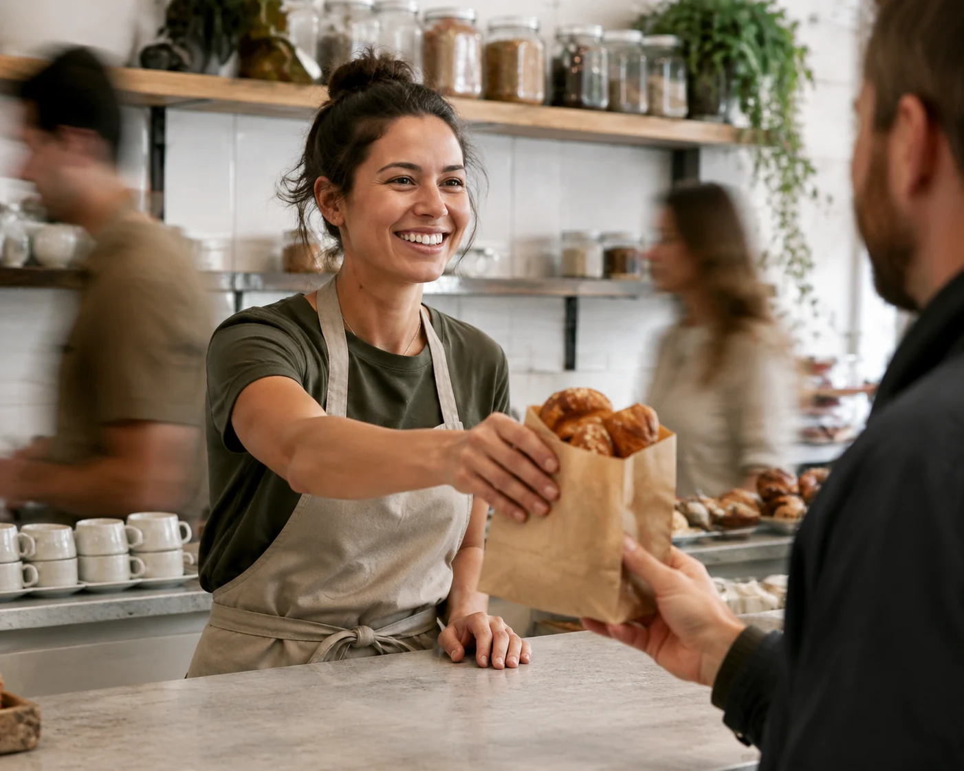 A cafe employee handing a pastry bag to a customer